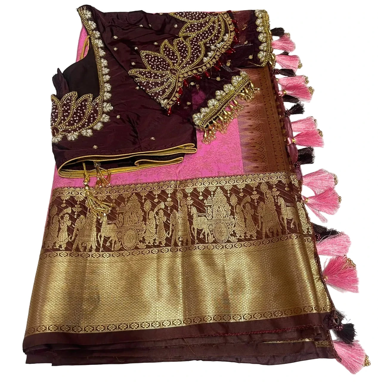 A folded traditional Indian ethnic wear fabric set featuring a deep maroon blouse with gold and silver zari embroidery and pearl accents, a bright pink inner fabric, and a wide gold brocade pallu with traditional motifs and pink tassels, displayed on a white marble-patterned surface.